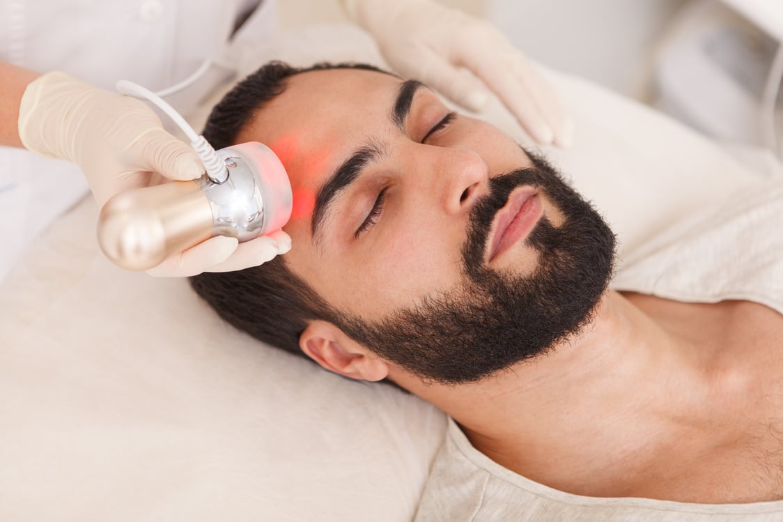 Attractive man relaxing while getting rf-lifting facial treatment at beauty clinic